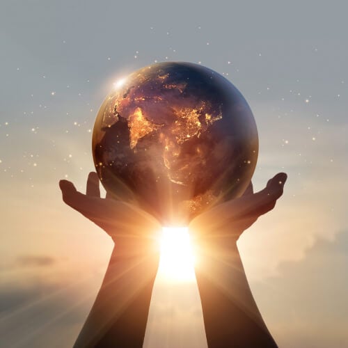 Hands uplift the Earth against a colorful sunset