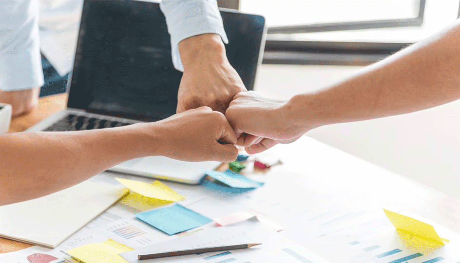 Team fist bump over table for business success